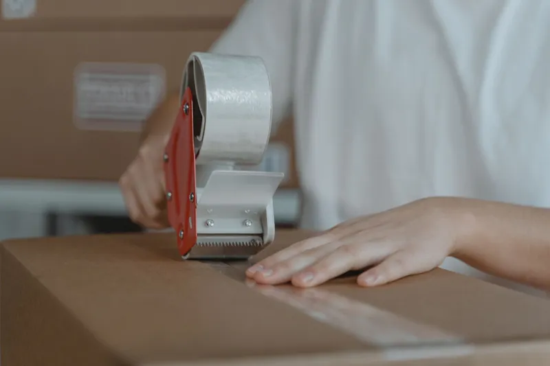A hand sealing a cardboard parcel with tape